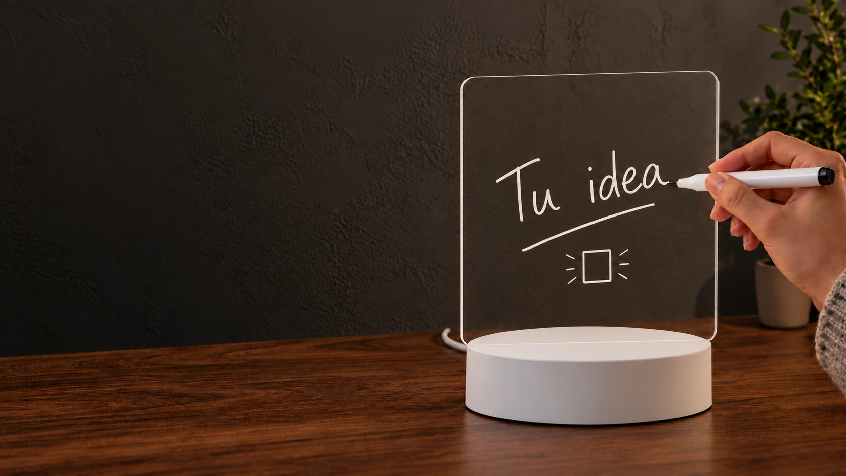 Una mano escribe «Tu idea» con el marcador sobre el panel apagado, antes de encender la lámpara.